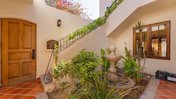 Un patio con puerta de madera, una escalera con plantas, una fuente de piedra y una ventana con vistas.