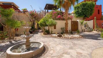 Un patio con una fuente de piedra, palmeras y plantas con flores.