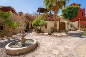 A courtyard with a stone fountain, palm trees, and flowering plants. - Amazing Home a few Steps to the Beach (  Loreto)