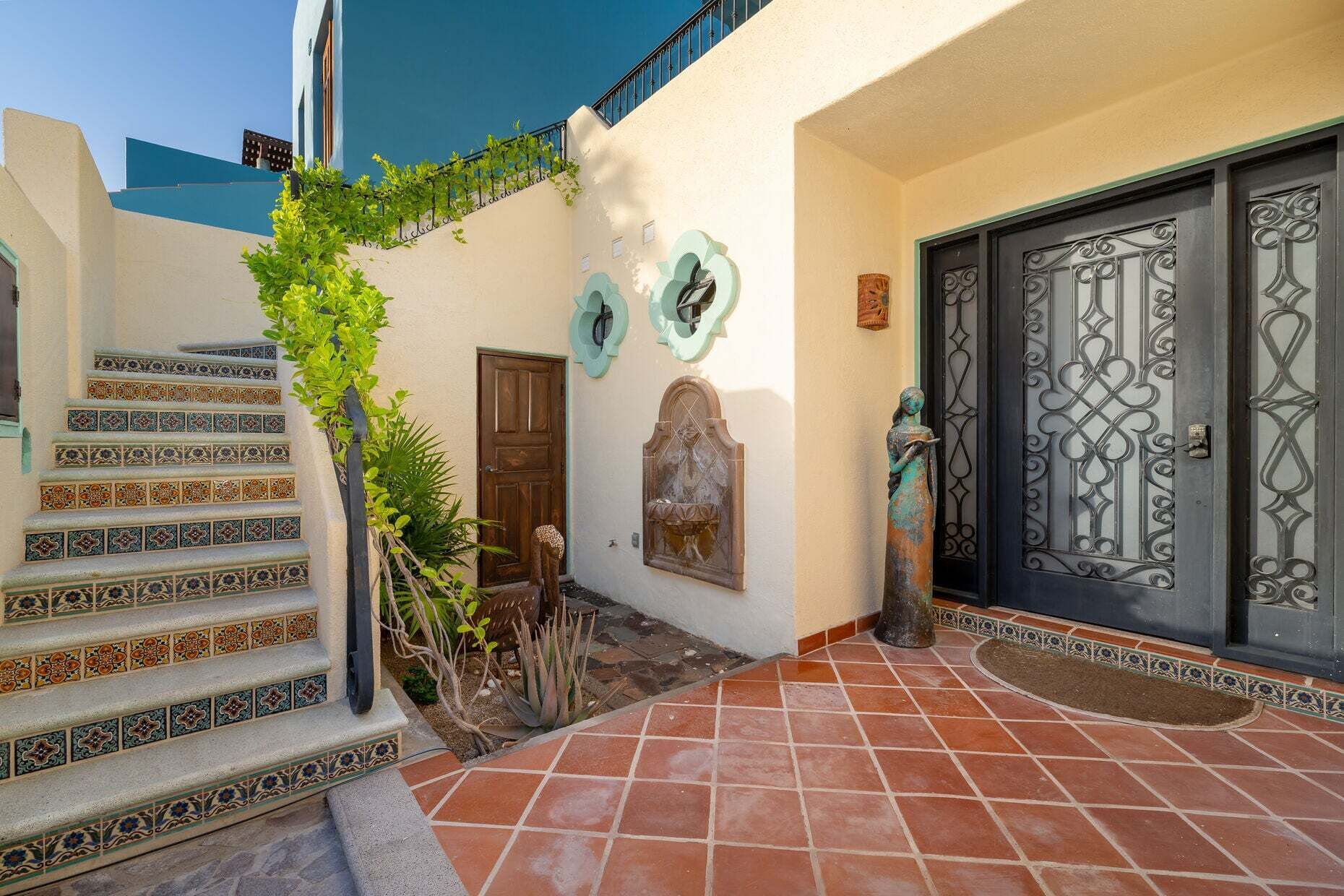 A building with a staircase, a door with decorative metalwork, and a small statue.