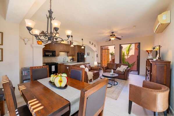 Uma sala de estar ampla com mesa de jantar, sofás de couro, um candelabro e um ventilador de teto.
