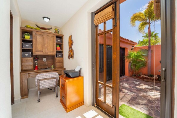 A room with a desk, shelves, a chair, a door leading to a courtyard with a palm tree and a stone pathway. - Stunning Home - Amazing Mountain Views (  Loreto)