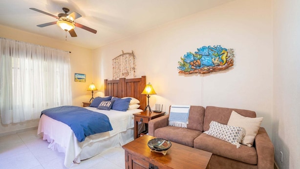 A bedroom with a bed, a wooden nightstand, a brown sofa, a wooden coffee table, a ceiling fan, and a wall decoration. - Stunning Home - Amazing Mountain Views (  Loreto)