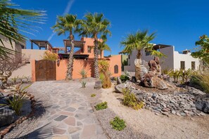 A courtyard with palm trees, a stone pathway, and a building with a traditional design. - Stunning Home - Amazing Mountain Views (  Loreto)