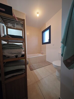 Ein Badezimmer mit einem Holzboden, der gefaltete Handtücher, eine Badewanne, eine Toilette und ein Fenster beherbergt.