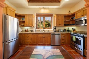 A kitchen with wooden cabinets, stainless steel appliances, a dishwasher, and a window with a view of greenery. - Water and Mountain Views-steps to Beach and Inn (  Loreto)
