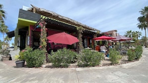 A restaurant with outdoor seating, covered by thatched roofs and red umbrellas, surrounded by greenery. - Our Exquisite Casa Offers a Perfect Blend of Comfort and Convenience ( Avenida punta sal Loreto)