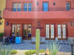 A building with a red facade, two wooden doors with glass panels, a balcony with a metal railing, and a cactus in the foreground. - Sweet Familiar Home a few Steps to Beach (  Loreto)