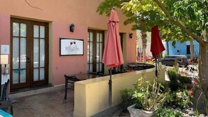 Un espacio al aire libre con mesas, un mostrador, un letrero y un árbol que da sombra.