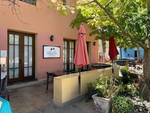 Un espacio al aire libre con mesas, un mostrador, un letrero y un árbol que da sombra.