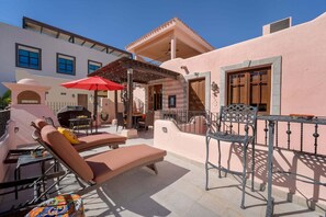 Eine Terrasss mit Lounge-Möbeln, einem roten Sonnenschirm und einem Grillplatz.