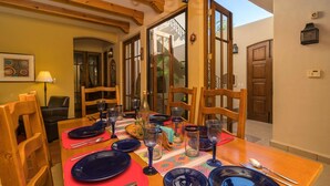 A dining table set with plates, glasses, and cutlery, wooden chairs, a chandelier, and a view of the outside. - Charming Home in Loreto Bay, Steps From the Golf Course and From Coffee Shop (  Loreto)