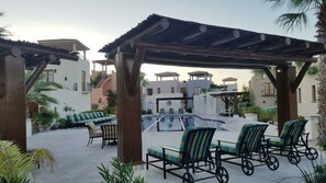 Ein Poolbereich mit Liegestühlen, einer Pergola und Blick auf Gebäude im Hintergrund.