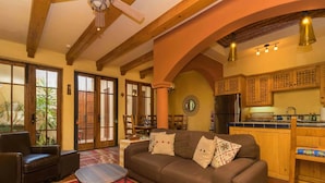 A cozy living room with a sofa, chairs, a small round table, and a kitchen area with wooden cabinets and a refrigerator. - Charming Home in Loreto Bay, Steps From the Golf Course and From Coffee Shop (  Loreto)