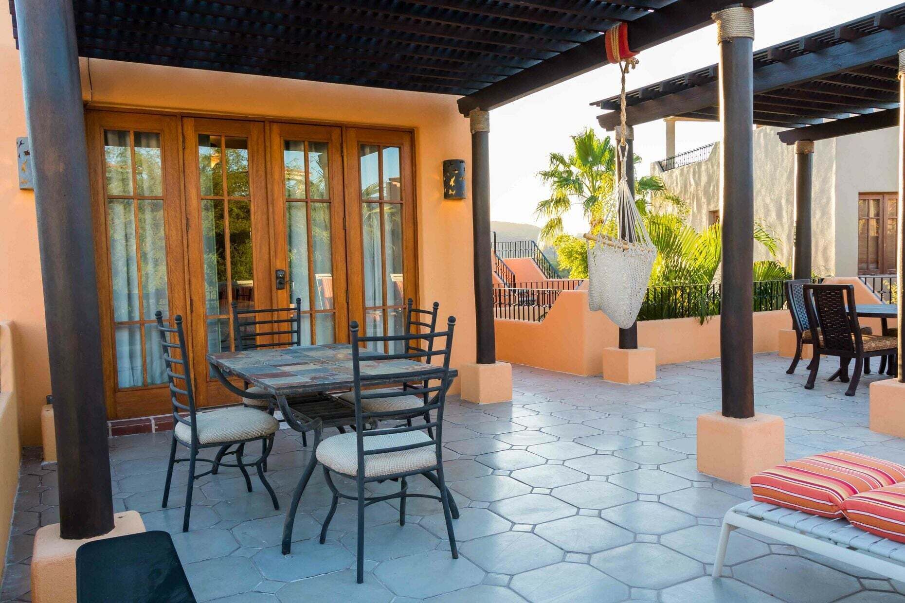 En uteplats med ett bord och stolar, en hängstol och ett takförsett område med en pergola.