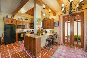 A kitchen with wooden cabinets, a black refrigerator, a tiled floor, and a bar area with stools. - Near the Beach! Wonderful House (  Loreto)