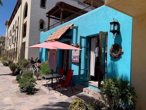 Un edificio con fachada azul, un balcón de madera, una mesa con sillas y un paraguas rojo.
