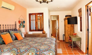 Un dormitorio con una colcha estampada, una puerta de madera, un televisor y una pequeña mesa con un cuenco.