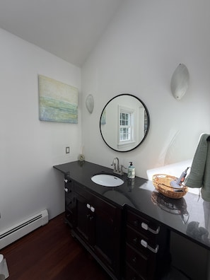 Un baño con un tocador negro, un espejo redondo, un lavabo blanco y un cuadro en la pared.