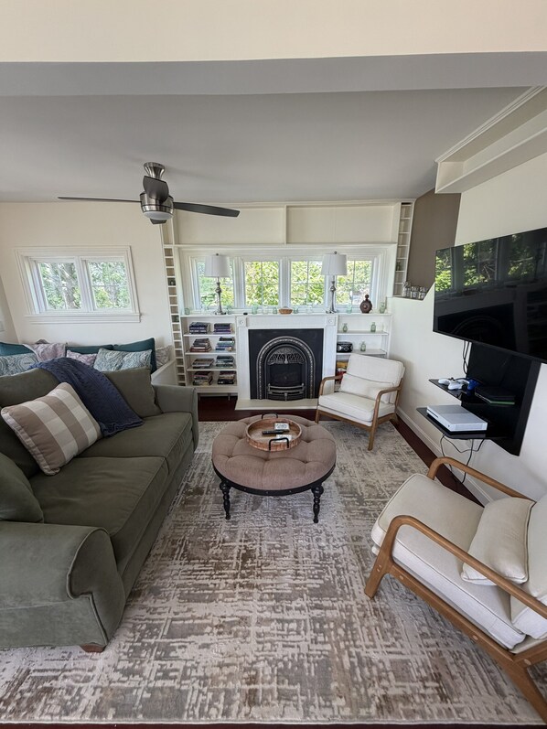 A living room with a sofa, armchair, round coffee table, fireplace, television, and bookshelves.