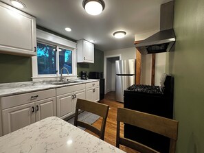 A kitchen with white cabinets, a stainless steel refrigerator, a gas stove, and a window with a view of trees. - Cozy 2-bedroom house in tranquil Chesterton with AC (Chesterton)