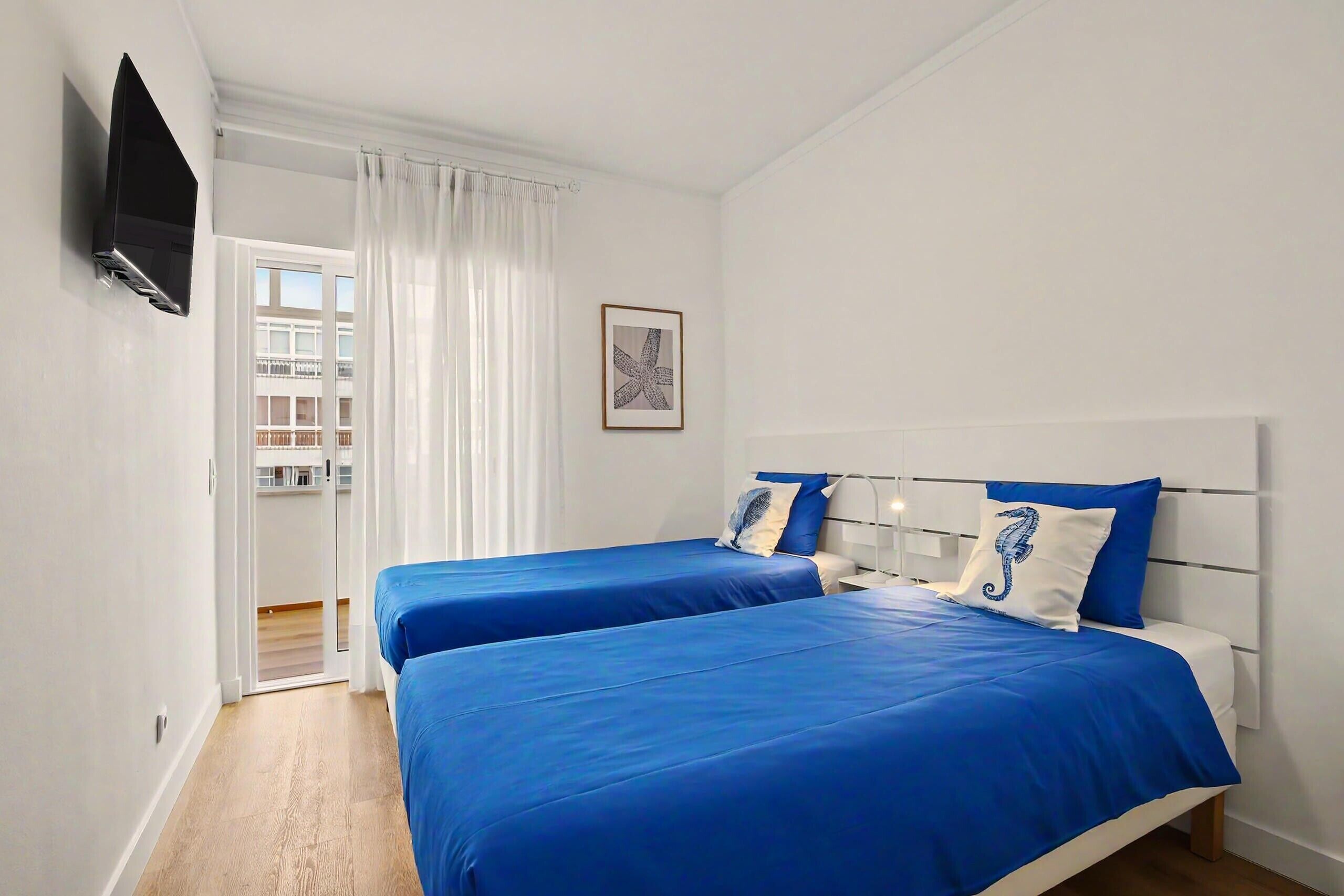 Een hotelkamer met twee bedden, een televisie, een raam met gordijnen en een ingelijste foto aan de muur.