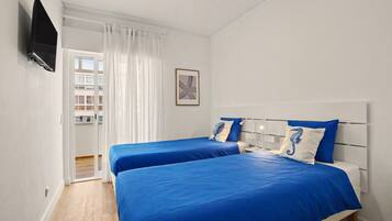 Een hotelkamer met twee bedden, een televisie, een raam met gordijnen en een ingelijste foto aan de muur.