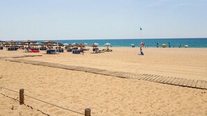 A beach with sun umbrellas, lounge chairs, and a lifeguard flag. - Apartment 40 Meters from the Beach with Balconies, Sea View, and Wi-Fi (Quarteira)