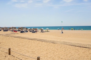 Een strand met zonneschermen, ligbedden en een strandwachtvlag.