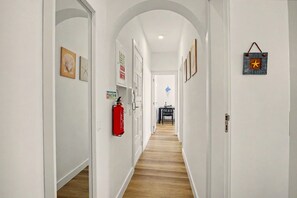 Een gang met witte muren, houten vloer en lijstwerken. Een brandblusser is aan de muur bevestigd en er hangt een decoratie.