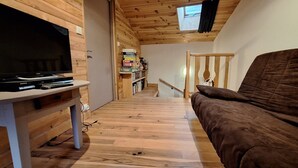 Een houten interieur met een televisie op een standaard, een bruine bank, een boekenkast en een trap.