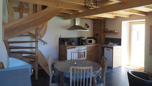 Een keuken met een centraal eiland, houten balken, een eettafel met stoelen en een trap.