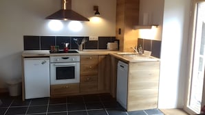 Een compacte keuken met een ingebouwde oven, een vaatwasser en een spoelbak. Er zijn kastjes en een aanrecht met diverse keukenbenodigdheden.