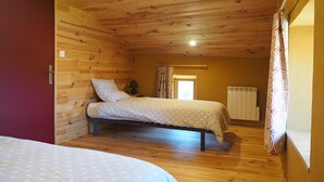 Een slaapkamer met een houten plafond, een bed, een nachtkastje, een radiator en een raam met gordijnen.