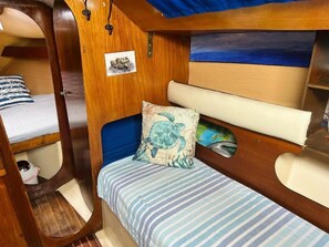 A cabin with a bed, a small shelf, a picture, and a view of the sea.