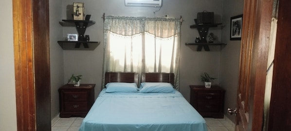 A bedroom with a bed, two nightstands, a window with curtains, and wall-mounted shelves. - Toronjal II Executive Suites (La Ceiba)