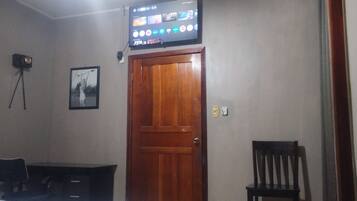 Een kamer met een houten deur, een bureau, een stoel, een tv en een lijst aan de muur.