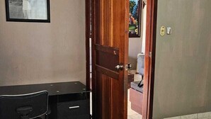 A bedroom with a bed, a desk with drawers, a chair, a television on the wall, and a door leading to another room. - Toronjal II Executive Rooms (La Ceiba)