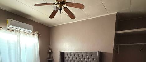 A bedroom with a bed, a ceiling fan, a table, and a chair.