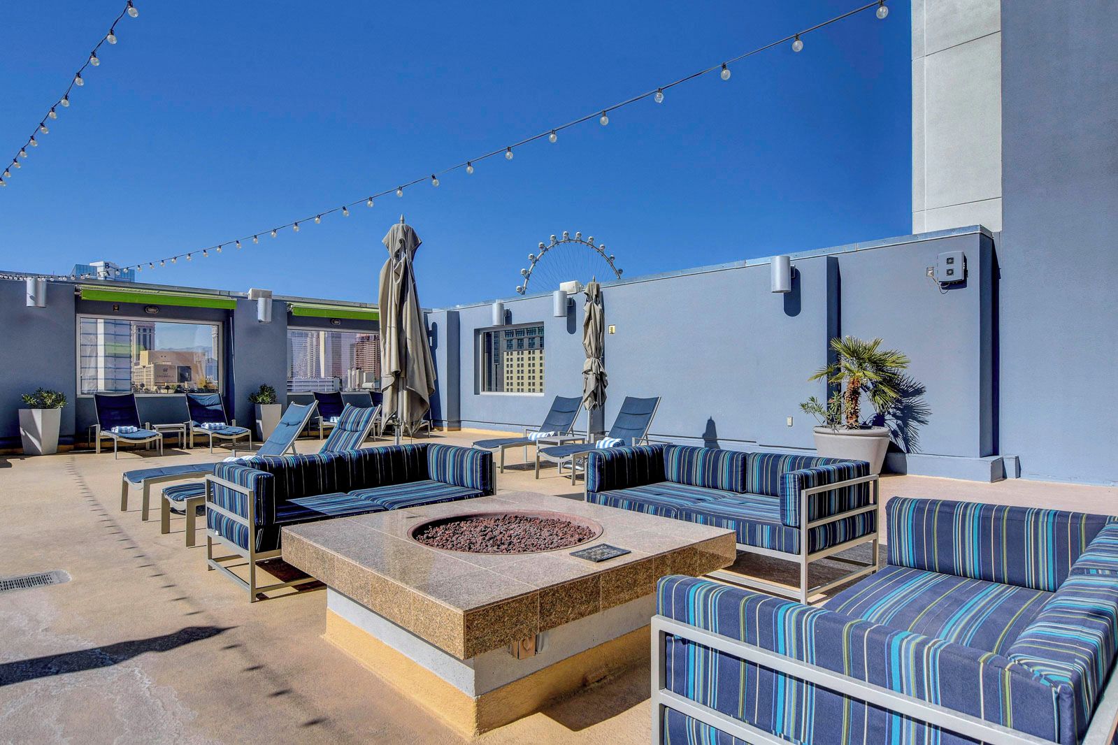 Eine Dachterrasse mit Sitzgelegenheiten im Freien, Lichterketten und einem Feuerkorb.