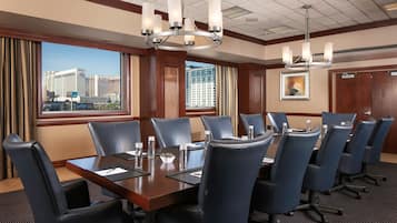 A conference room with a large table, multiple chairs, and a view of buildings through the windows.