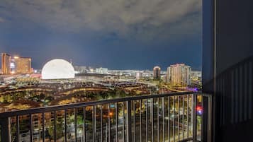 A balcony with a view of a cityscape at night, including buildings and a large illuminated dome structure.