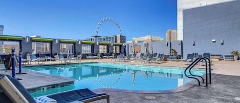 A rooftop pool area with lounge chairs, a pool, and a Ferris wheel in the background.
