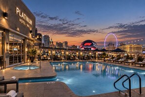 Un hotel con piscina, sillas de descanso y vistas del horizonte urbano al atardecer.