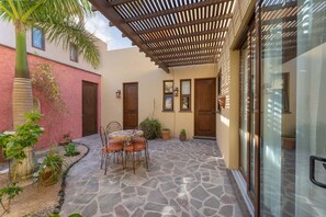 Un patio con suelo de piedra, una pérgola de madera, una mesa con sillas y un ventanal de vidrio.