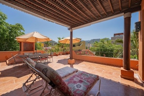 Un patio techado al aire libre con asientos, sombrillas y vistas del paisaje circundante.