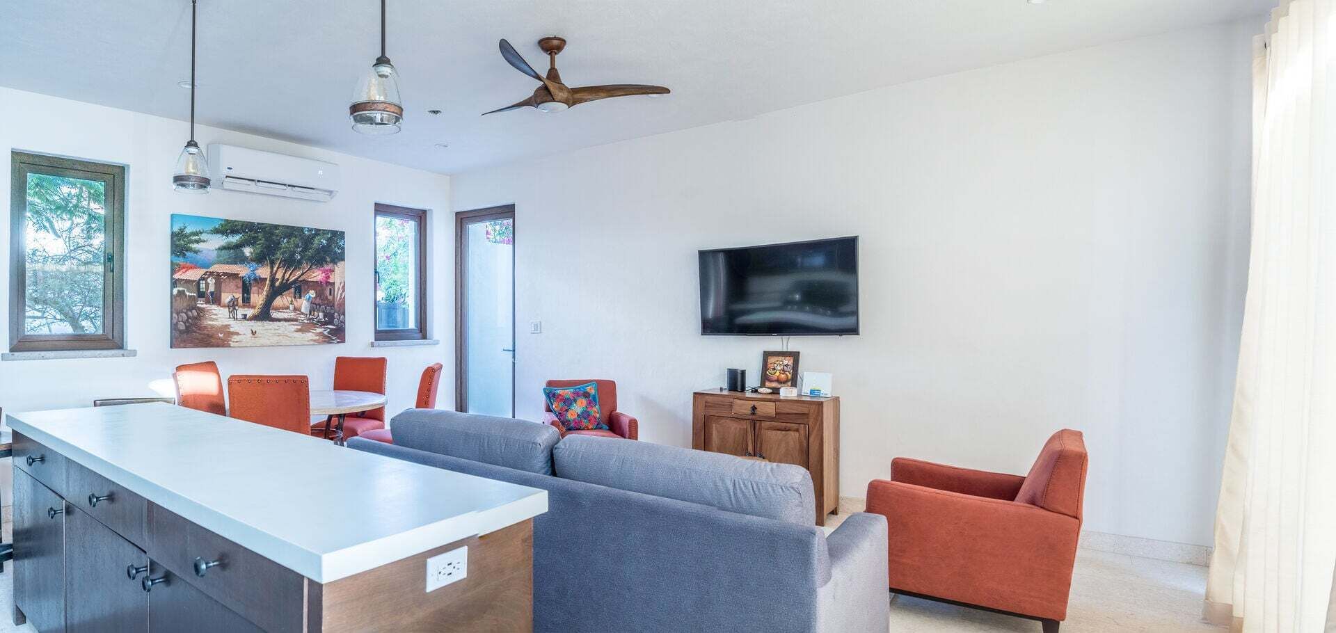 Ein modernes Wohnzimmer mit einer Couch, Sesseln, einem Fernseher und einem Deckenventilator.
