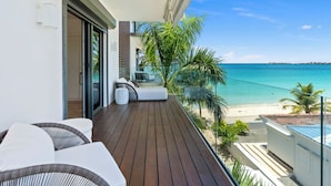 Ein Balkon mit Holzboden, einer weißen Wand und Blick auf den Strand.