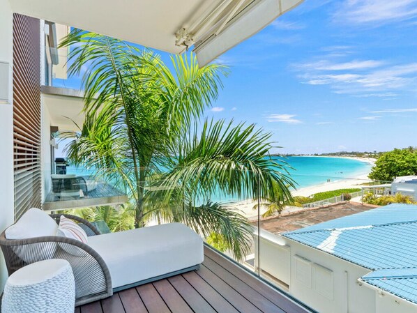 Ein Balkon mit Blick auf einen Strand, einem weißen Sofa und einem Glastisch.