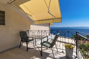 Ein Balkon mit Tisch, Stühlen, einer Topfpflanze und Blick aufs Meer.
